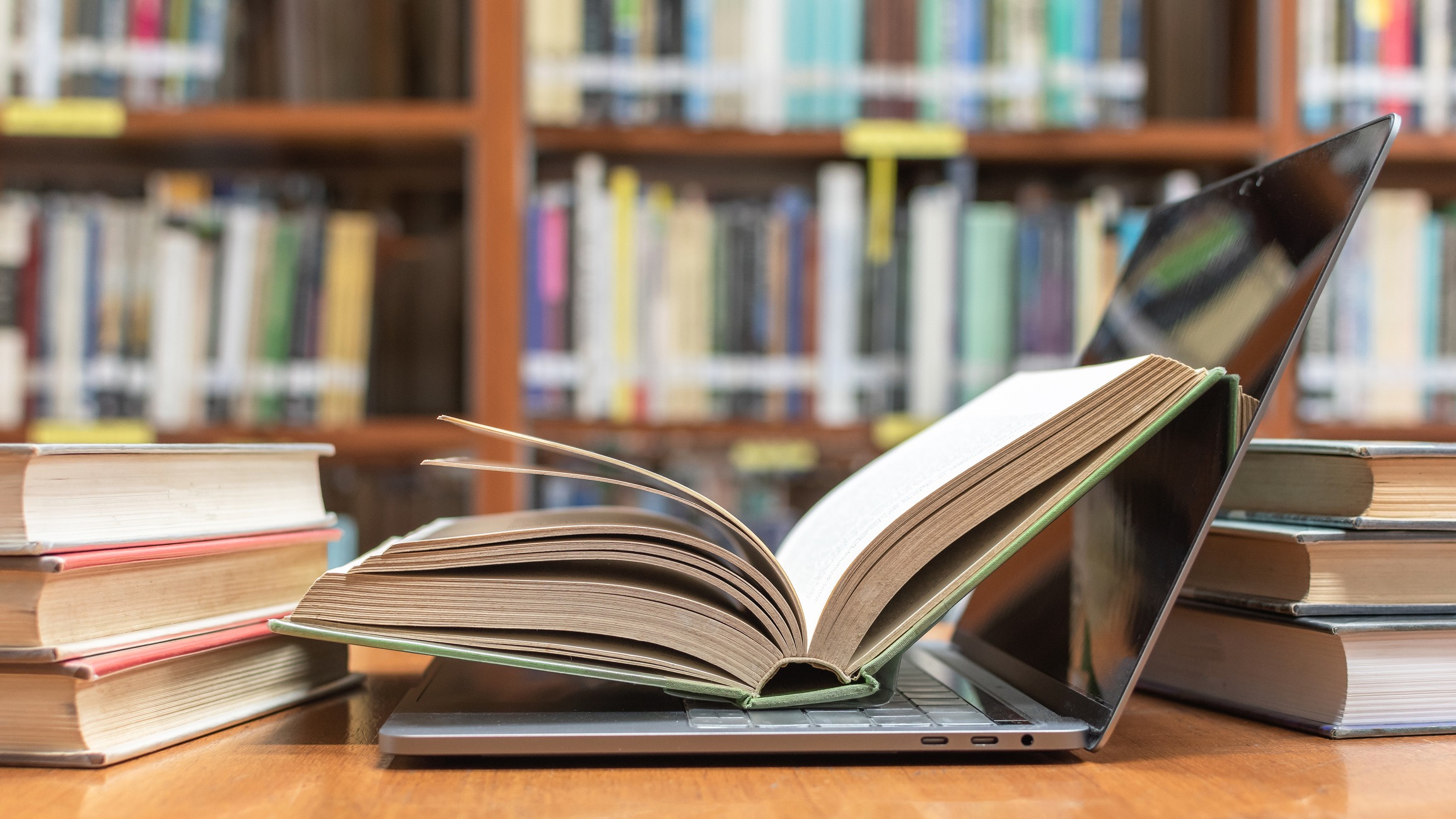open book sitting on open laptop next to stacks of books
