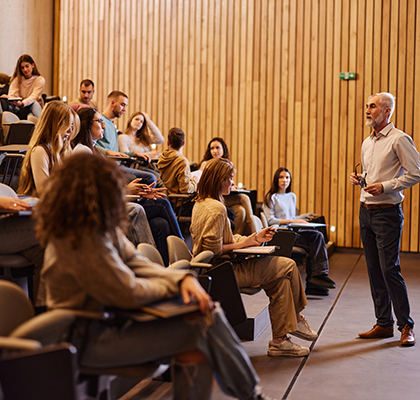 Senior professor talking in front of large group of his students during a lecture in amphitheater. Copy space.